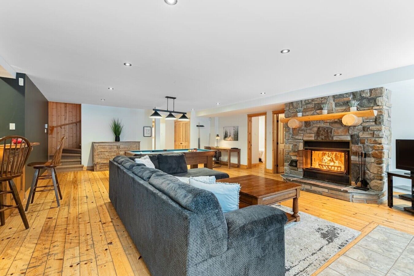 A modern living room with a stone fireplace, a pool table, and a cozy seating area.