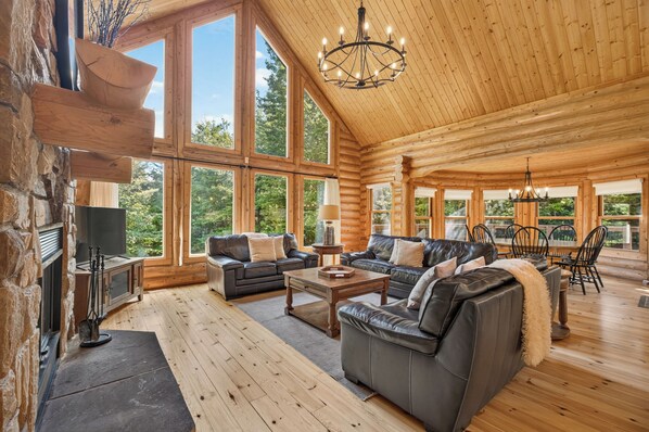 L’intérieur de cette vaste cabane en rondins est agrémenté d’une cheminée, de canapés en cuir, d’un coin repas et de grandes fenêtres qui offrent une vue sur le paysage extérieur.