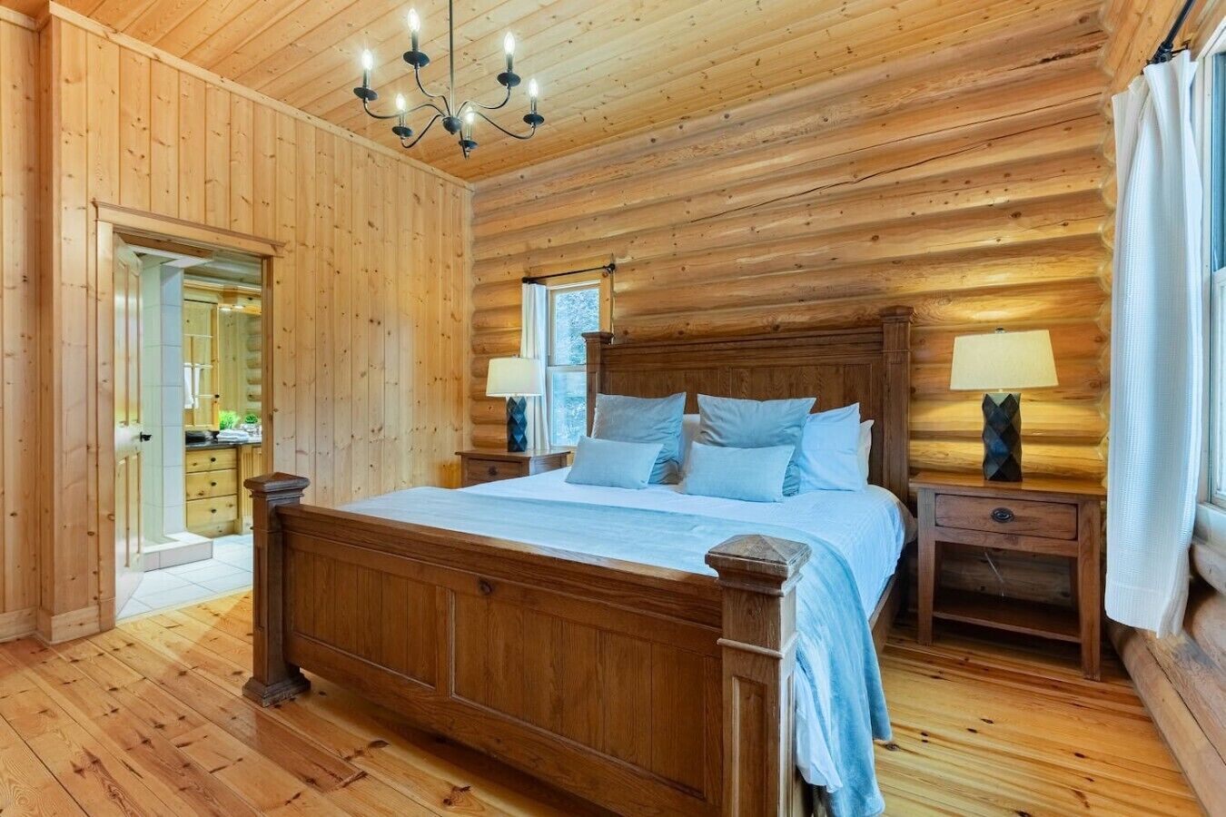 Une chambre aux murs lambrissés, avec un grand lit, deux tables de chevet dotées de lampes et un lustre.