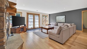 A spacious living room with a stone fireplace, a large flat-screen TV, a sectional sofa, and a dining table.