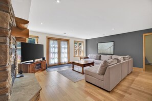 A spacious living room with a stone fireplace, a large flat-screen TV, a sectional sofa, and a dining table. - Fiddler Lake Resort - Deer 48 (Mille-Isles)