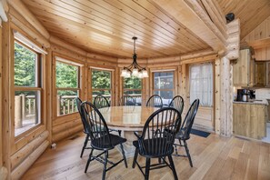A wooden interior with a round dining table surrounded by chairs, large windows, and a kitchen area. - Fiddler Lake Resort - Deer 48 (Mille-Isles)