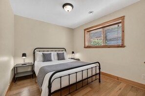 A bedroom with a bed, bedside tables, a window with blinds, and a ceiling light.