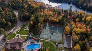 An aerial view of a property with a tennis court, swimming pool, and a lake surrounded by autumn-colored trees.