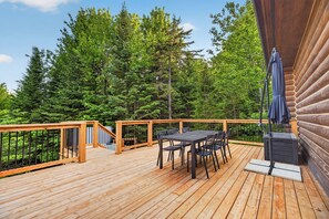 A wooden deck with a table and chairs, surrounded by a wooden railing, overlooking a forest. - Fiddler Lake Resort - Rabbit 57 (Mille-Isles)