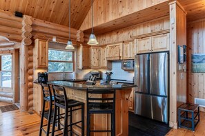 A log cabin kitchen with a central island, bar stools, stainless steel appliances, and wooden cabinetry. - Fiddler Lake Resort - Rabbit 57 (Mille-Isles)