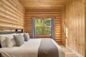 A log cabin bedroom with a bed, curtains, and a window. - Fiddler Lake Resort - Rabbit 57 (Mille-Isles)