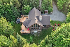 A cabin with a deck, a chimney, and a gravel driveway surrounded by trees. - Fiddler Lake Resort - Rabbit 57 (Mille-Isles)
