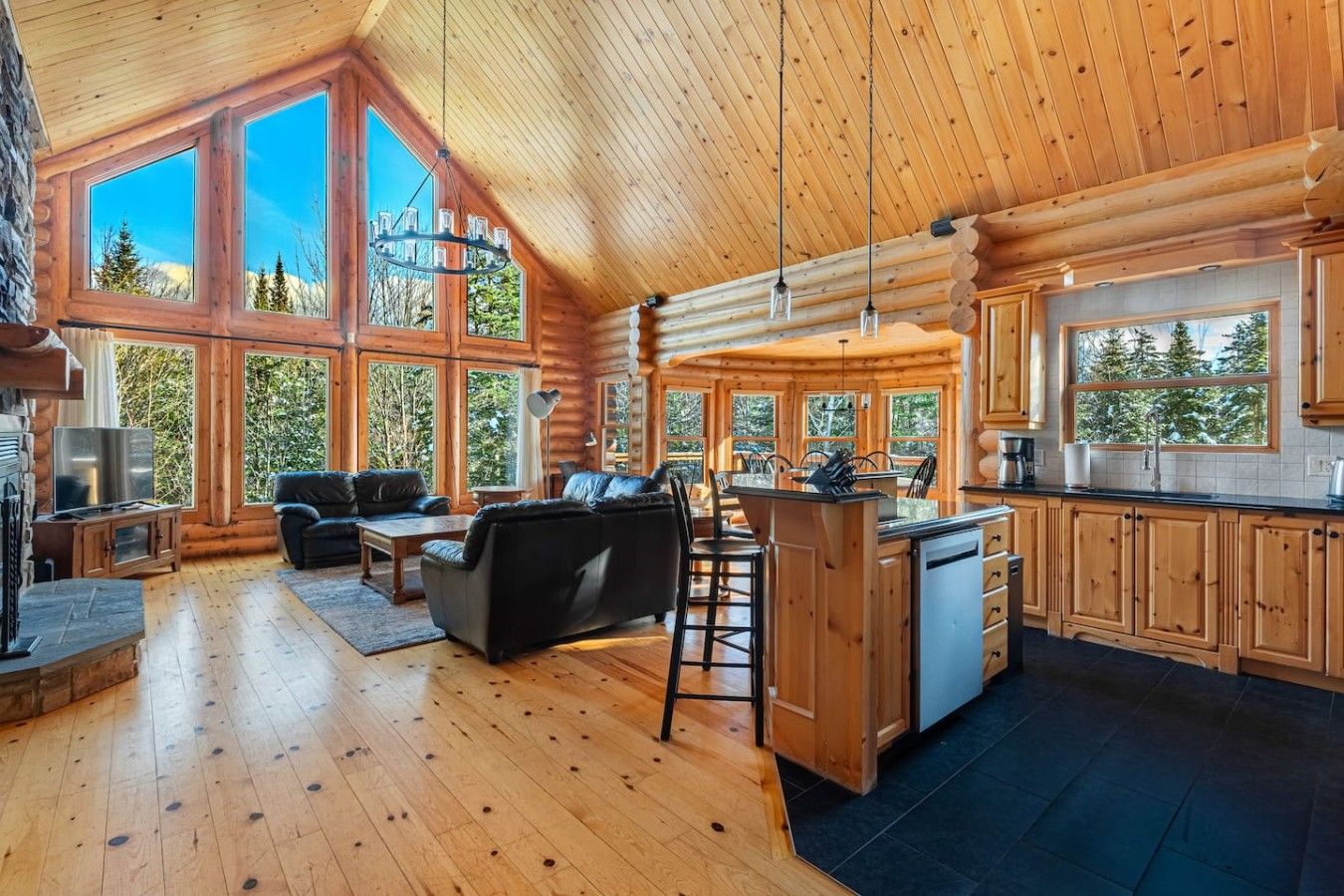 A log cabin interior with a living area, kitchen, and large windows.