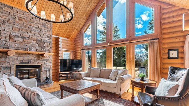 A log cabin interior with a stone fireplace, a television, a sofa, and a large window offering a view of the outdoors. - Fiddler Lake Resort - Deer 86 (Mille-Isles)