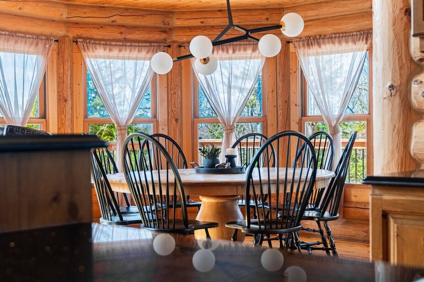 A wooden cabin interior with a dining table, chairs, and a hanging light fixture.