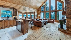 Ein rustikales Holzhaus-Interieur mit Küche, Essbereich und Wohnzimmer, ausgestattet mit großen Fenstern und Holzdielen.
