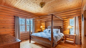 Ein Schlafzimmer in einer Blockhütte mit einem Himmelbett, einem Nachttisch und einem Fenster.