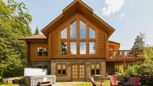 Eine Blockhütte mit einer großen Veranda, einer Holzterrasse und einem Kamin aus Stein.