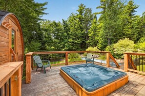 A wooden deck with a hot tub, chairs, and a pool.