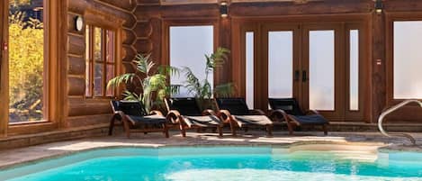 A pool area with wooden walls, large windows, and lounge chairs.