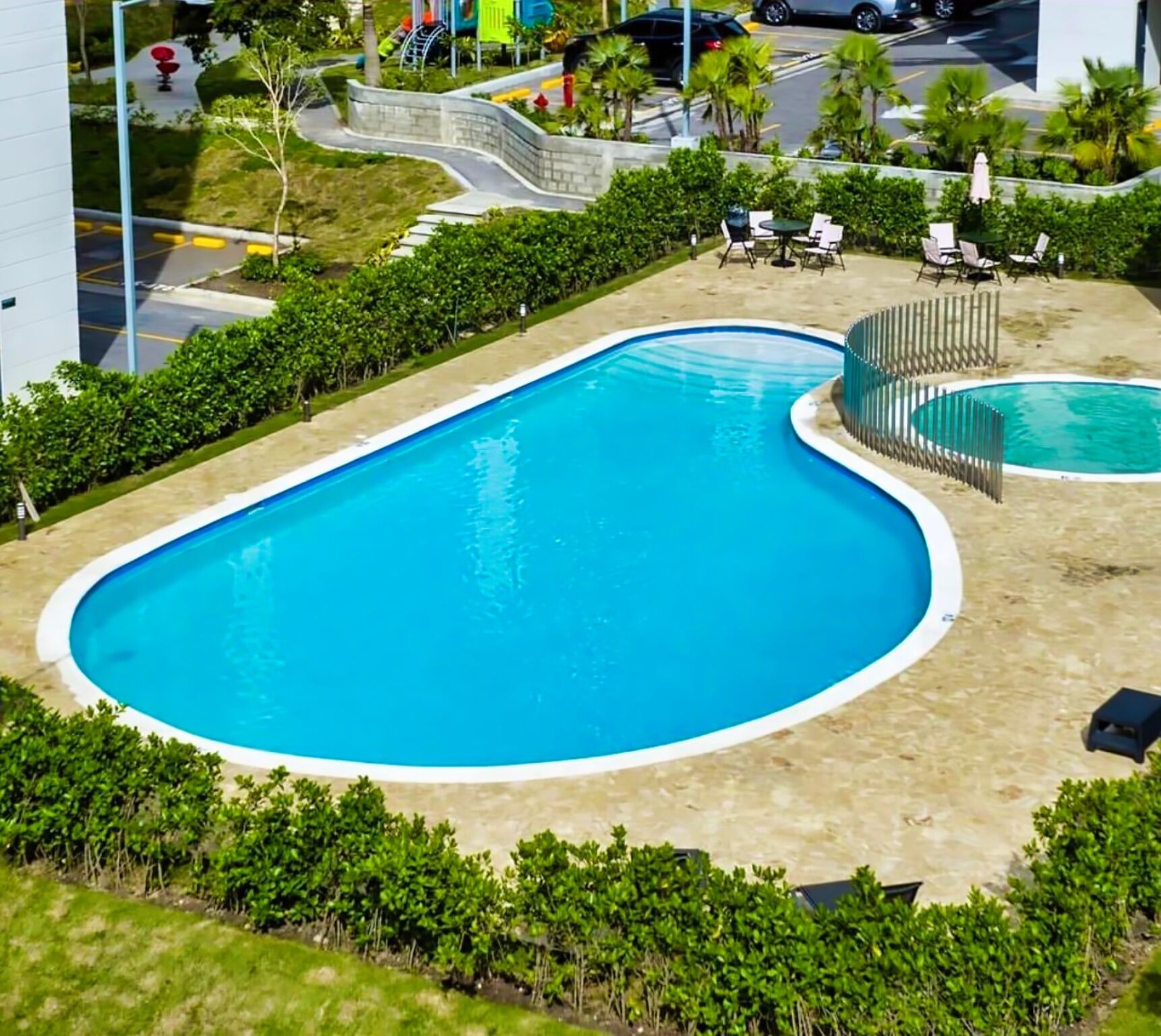 A swimming pool with a curved design, surrounded by a low hedge and a paved deck.