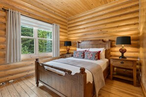 Ein Schlafzimmer einer Holzhütte mit einem Bett, zwei Nachttischen, einem Fenster und Vorhängen.