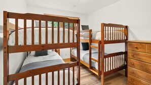 Une pièce avec deux lits superposés, une commode en bois et un luminaire fixé au plafond.