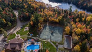 Vue aérienne d’un complexe hôtelier doté d’un court de tennis, d’une piscine et d’un lac entouré d’arbres aux couleurs automnales.