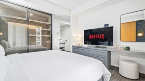 Una habitación de hotel moderna con una cama grande, un televisor montado en la pared, un escritorio con computadora y un armario.