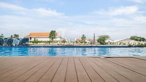 Una terraza de madera frente a una piscina con edificios al fondo.