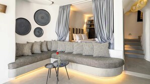 A modern living room with a curved sofa, a small round table, and a staircase leading to an upper level. - Deep Earth Villas (Santorini)
