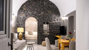 A modern interior with a stone archway, a sofa, a dining table with chairs, and a small table with a lamp. - Deep Earth Villas (Santorini)