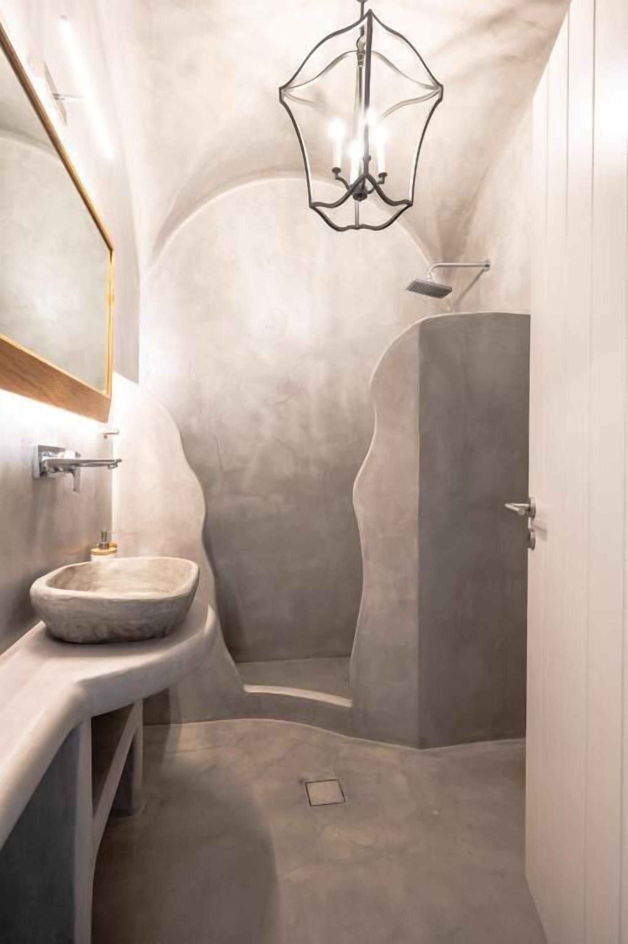 Een badkamer met een stenen wastafel, een spiegel en een douchehoek.