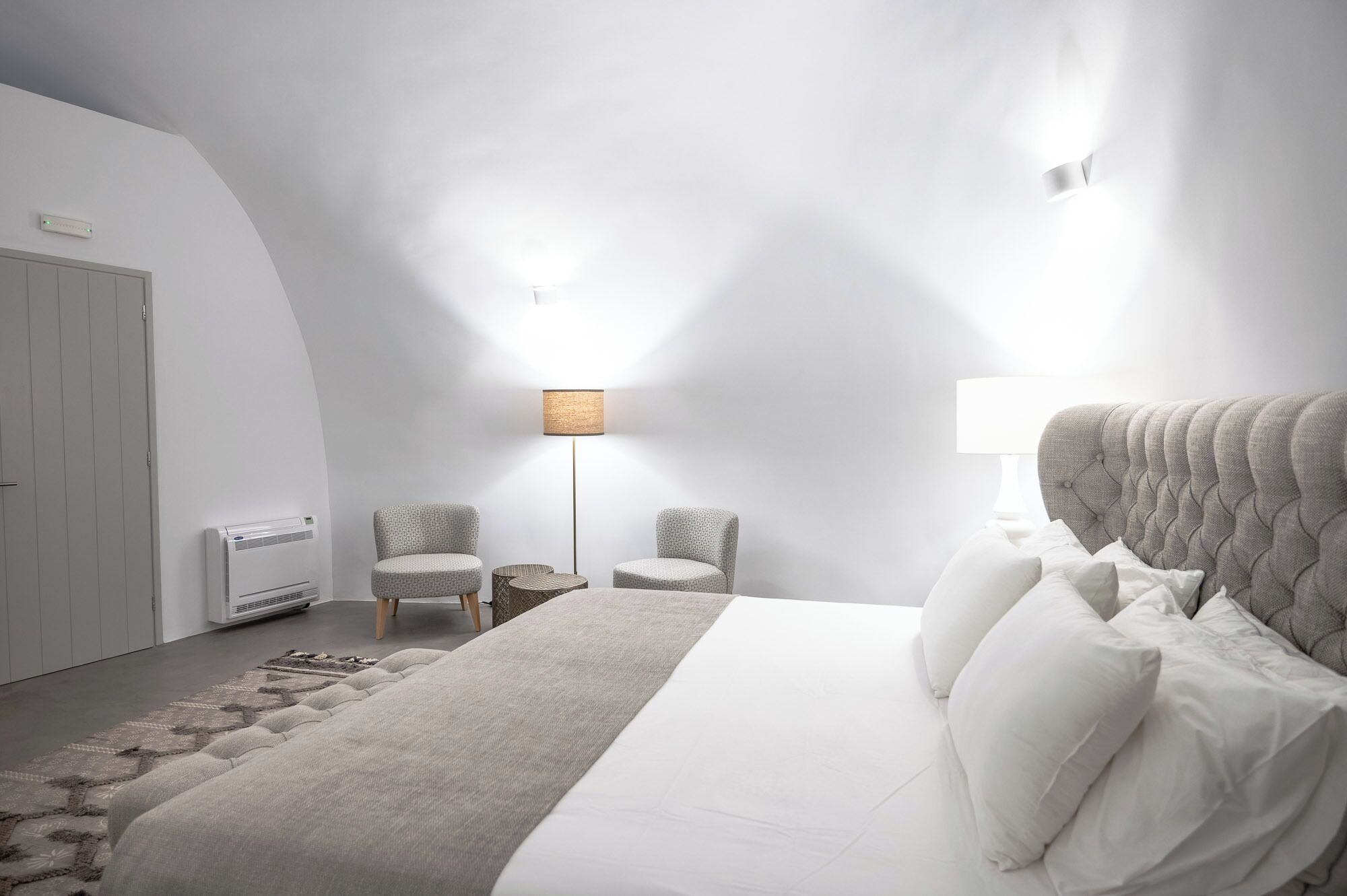 A modern bedroom with a large bed, two chairs, a floor lamp, and a radiator.