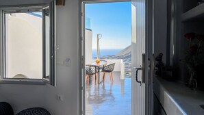 A modern kitchen with a view of the sea, a dining area with a table and chairs, and a living area with a sofa. - Deep Earth Villas (Santorini)