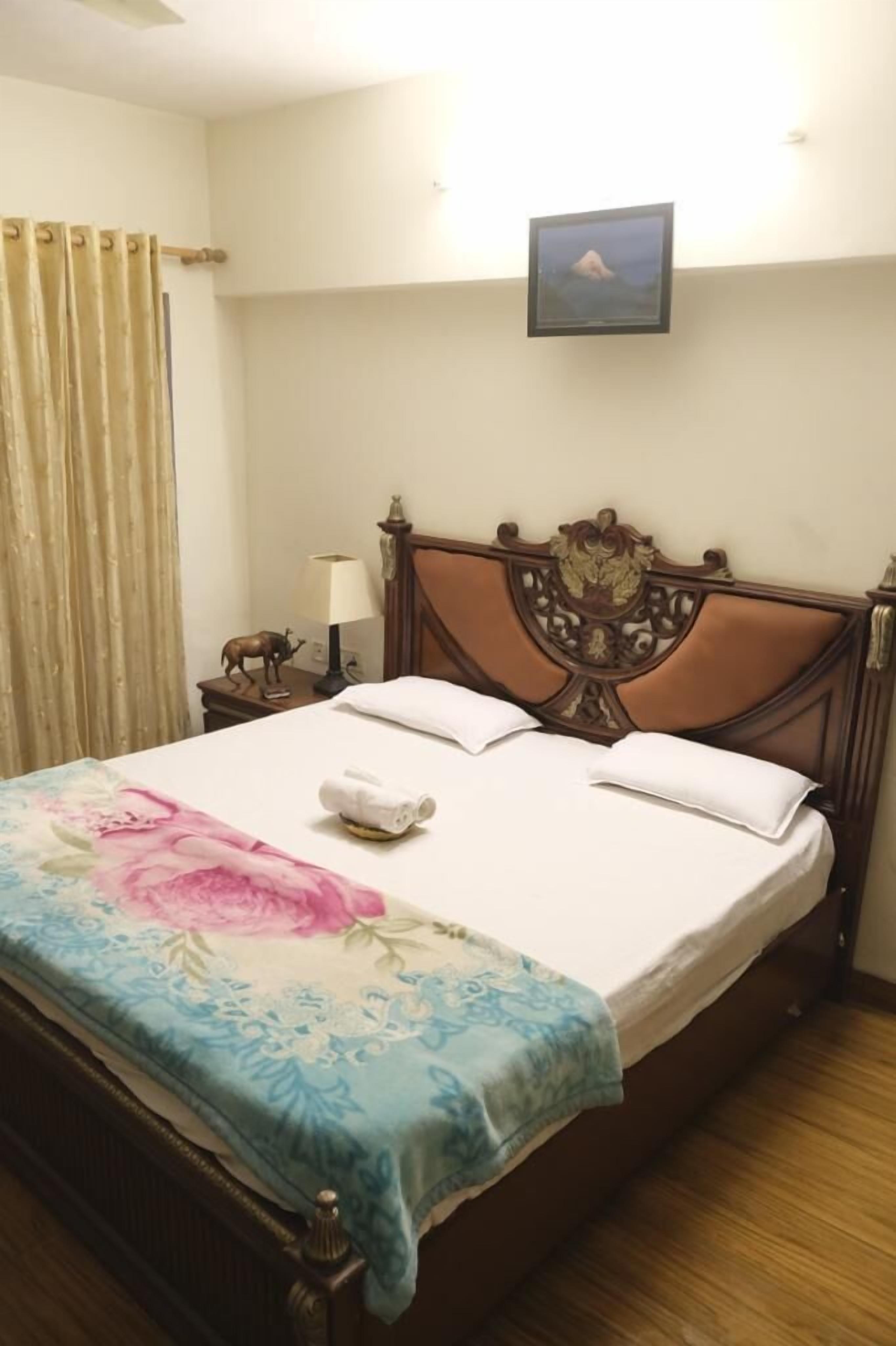 A neatly made bed with a floral bedspread, a wooden headboard, and a small bedside table with a lamp and a decorative item.
