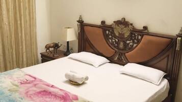 A neatly made bed with a floral bedspread, a wooden headboard, and a small bedside table with a lamp and a decorative item.