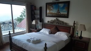 Un lit bien fait, avec du linge de lit blanc et une tête de lit décorative, une table de chevet avec une lampe, et un tableau représentant la Tour Eiffel accroché au mur.