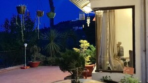 Un espace patio extérieur avec une table ronde et des chaises, entouré de plantes en pot et agrémenté d’une lanterne suspendue.