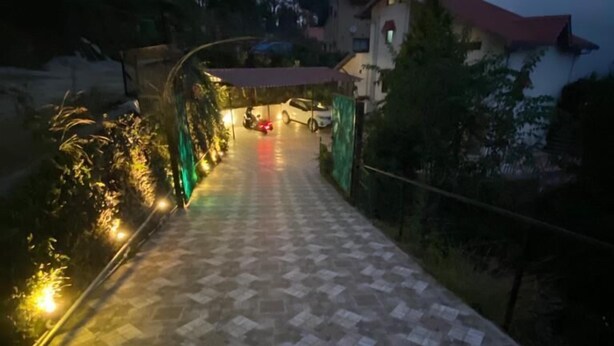 Un chemin pavé mène à un bâtiment doté d’un toit rouge, qui est entouré de verdure.