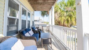 A covered porch with wicker furniture and a view of a building in the background. - A Kure for the Sol (Kure Beach)