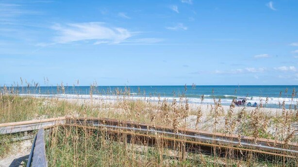 A beach view with a wooden boardwalk, beach grass, and the ocean. - A Kure for the Sol (Kure Beach)