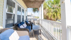 Eine überdachte Veranda mit Korbmöbeln und einem Tisch, mit Blick auf eine Palme und ein Gebäude im Hintergrund.