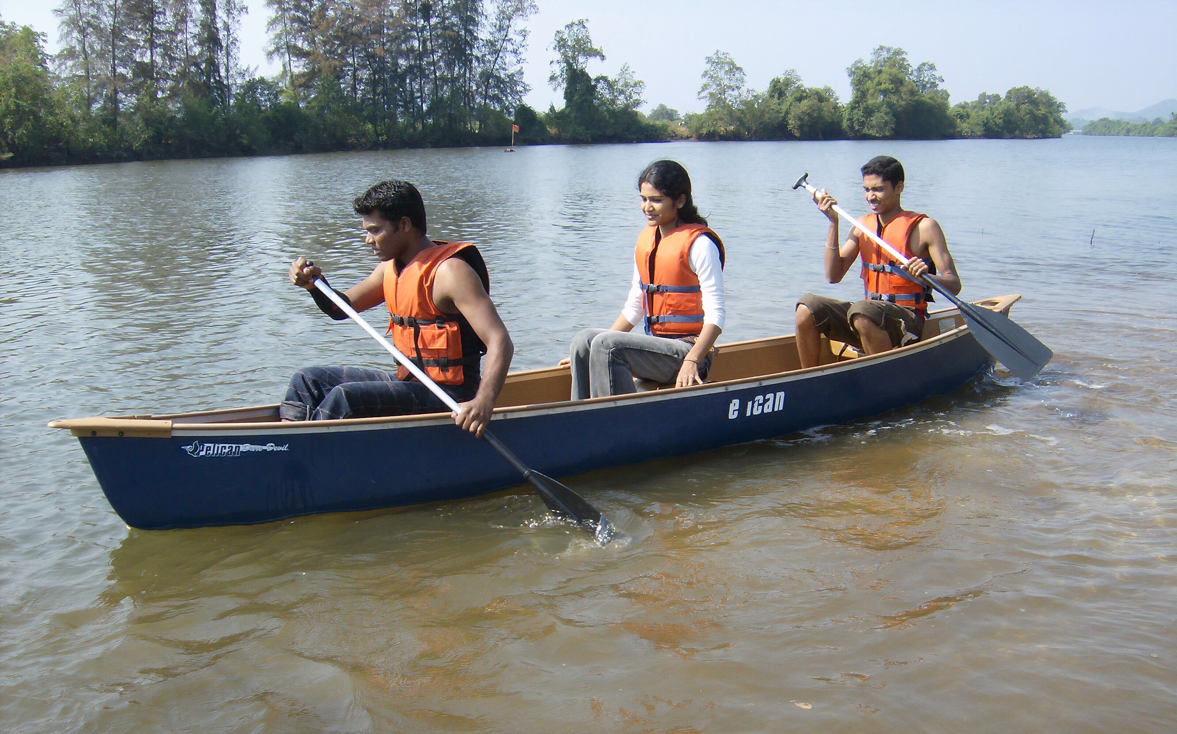 Une barque à rames avec trois personnes portant des gilets de sauvetage, naviguant sur une étendue d’eau calme.