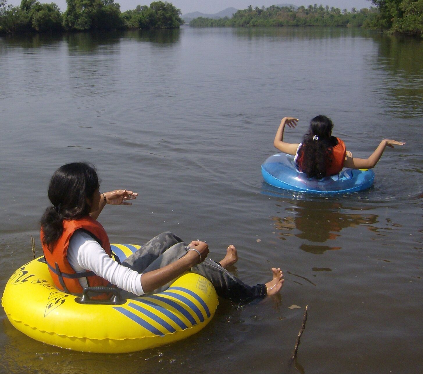 Zwei Personen auf Wasserschläuchen in einem ruhigen Fluss.