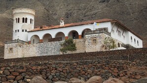 A white building with a tower, stone walls, and a rocky foreground. - El Ático Bonito Das Schöne Penthouse am Meer (Las Playitas)