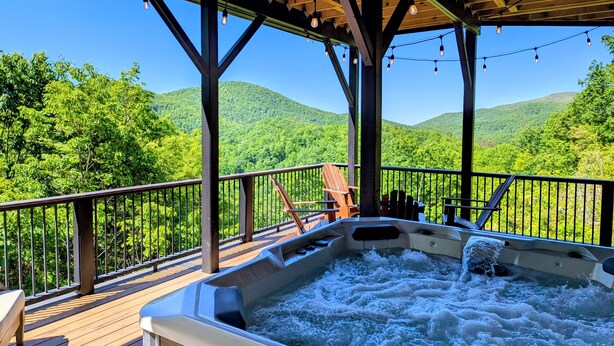 Un jacuzzi en una terraza de madera con vistas a colinas verdes.