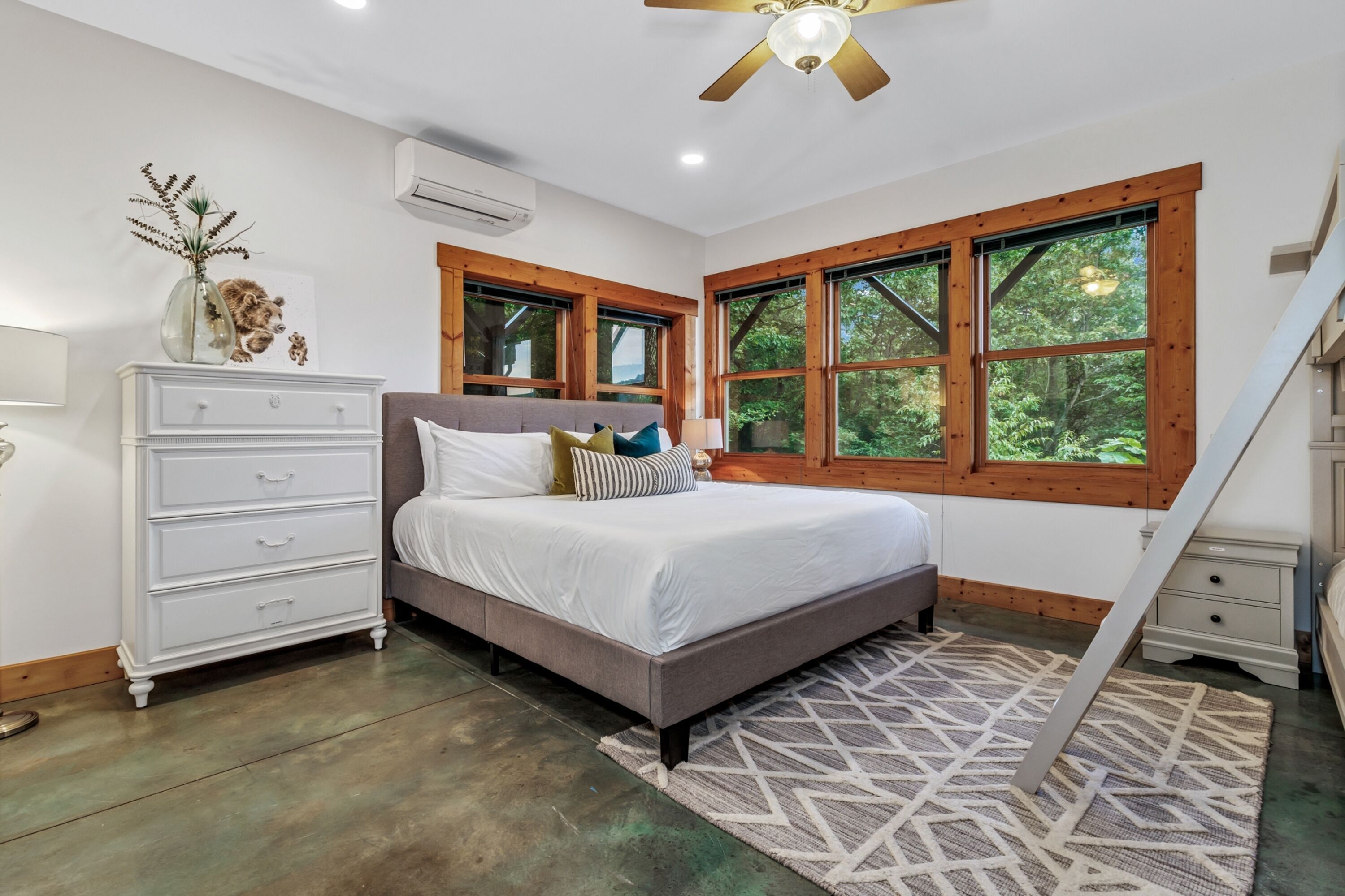 A bedroom with a bed, dresser, and large windows.