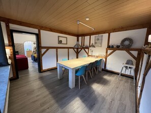 A dining area with a wooden table and chairs, a kitchen in the background, and a view of the living room. - Platell Ferienhäuser Lerbach, Detached house for up to 8 people with fireplace (Osterode am Harz)
