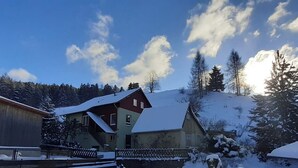 A two-story house with a snow-covered roof, surrounded by a wooden fence and snow-covered ground. - Platell Ferienhäuser Lerbach, Detached house for up to 8 people with fireplace (Osterode am Harz)