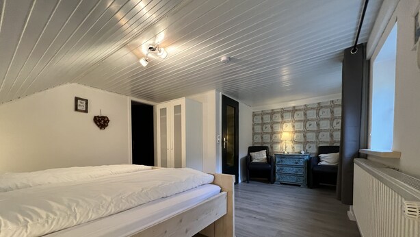 A bedroom with a bed, a dresser, a chair, and a radiator. - Platell Ferienhäuser Lerbach, Detached house for up to 8 people with fireplace (Osterode am Harz)