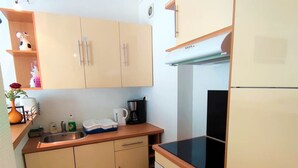 A compact kitchen with beige cabinets, a black stove, and a sink. - Appart T3 Tout Confort + Parking Privatif (La Rochelle)