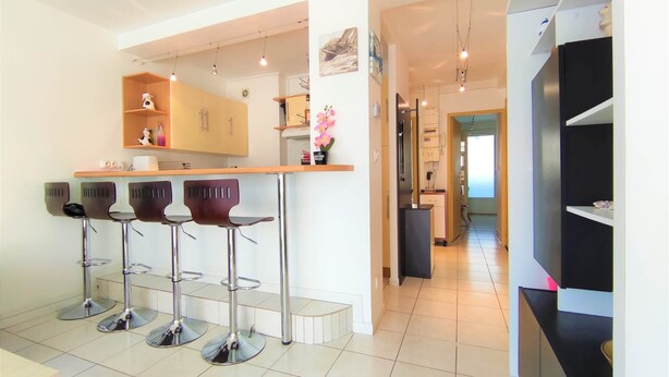 A modern kitchen with a bar area, stainless steel appliances, and a view into the dining area. - Appart T3 Tout Confort + Parking Privatif (La Rochelle)