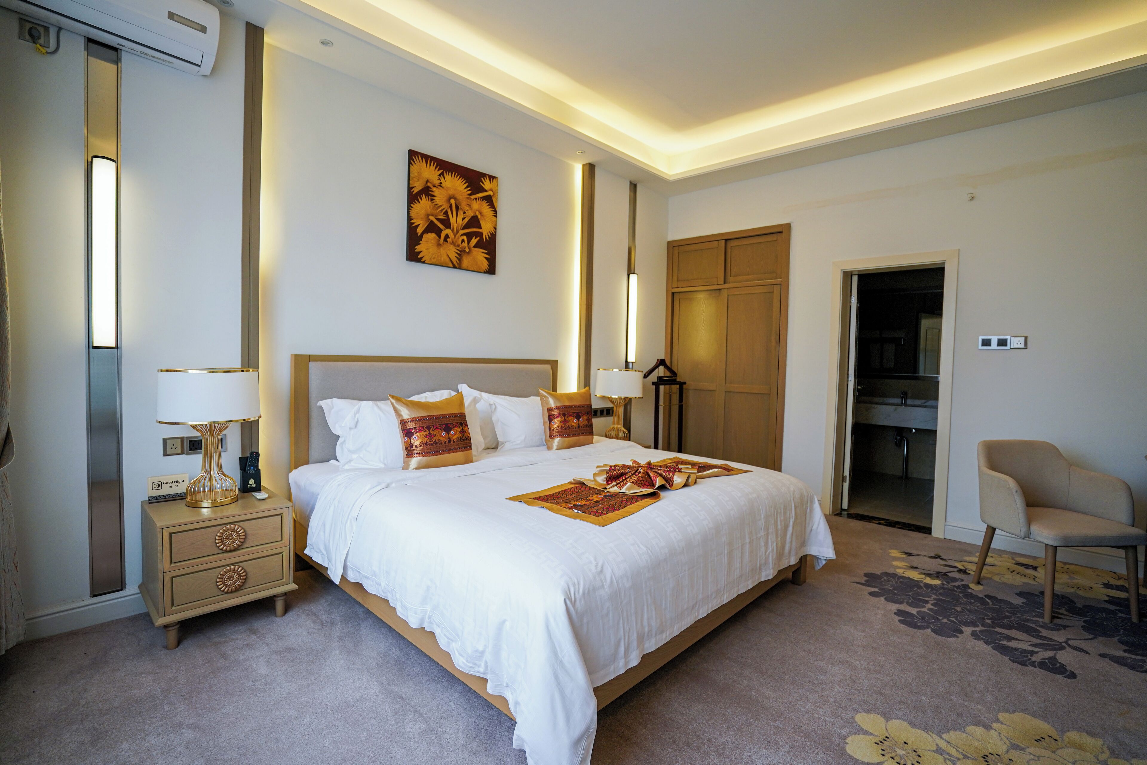 A well-lit bedroom with a large bed, bedside tables, a chair, and a wardrobe.